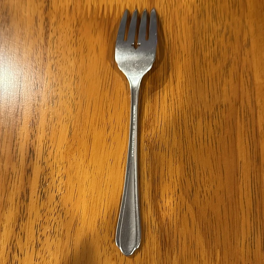 Oneida Tudor plate silver salad fork. Neck is rounded and has a slit edge.